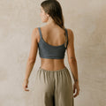 Woman wearing a gray sports bra and beige linen pants against a beige wall