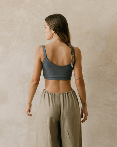 Woman wearing a gray sports bra and beige linen pants against a beige wall